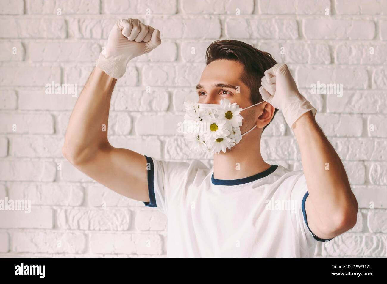 Portrait de médecin gai masculin dans un masque protecteur de fleur célébrant la victoire contre le coronavirus. Jeune homme heureux dans le masque médical avec Marguerite fl Banque D'Images