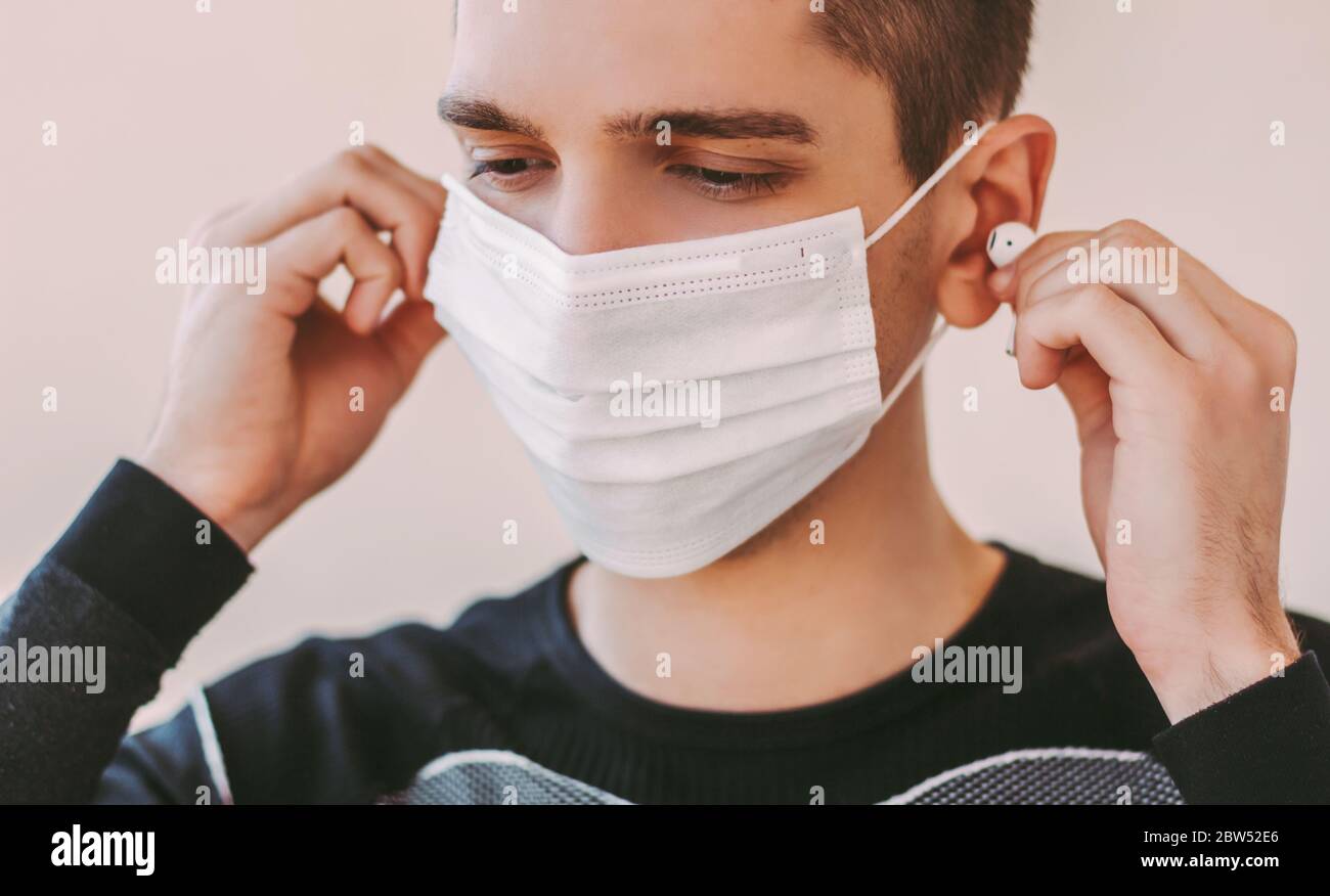 Joyeux jeune sportif homme en masque médical de protection Ecouter de la musique avec des écouteurs sans fil bluetooth. Entraîneur de fitness professionnel à la quarantaine à domicile Banque D'Images