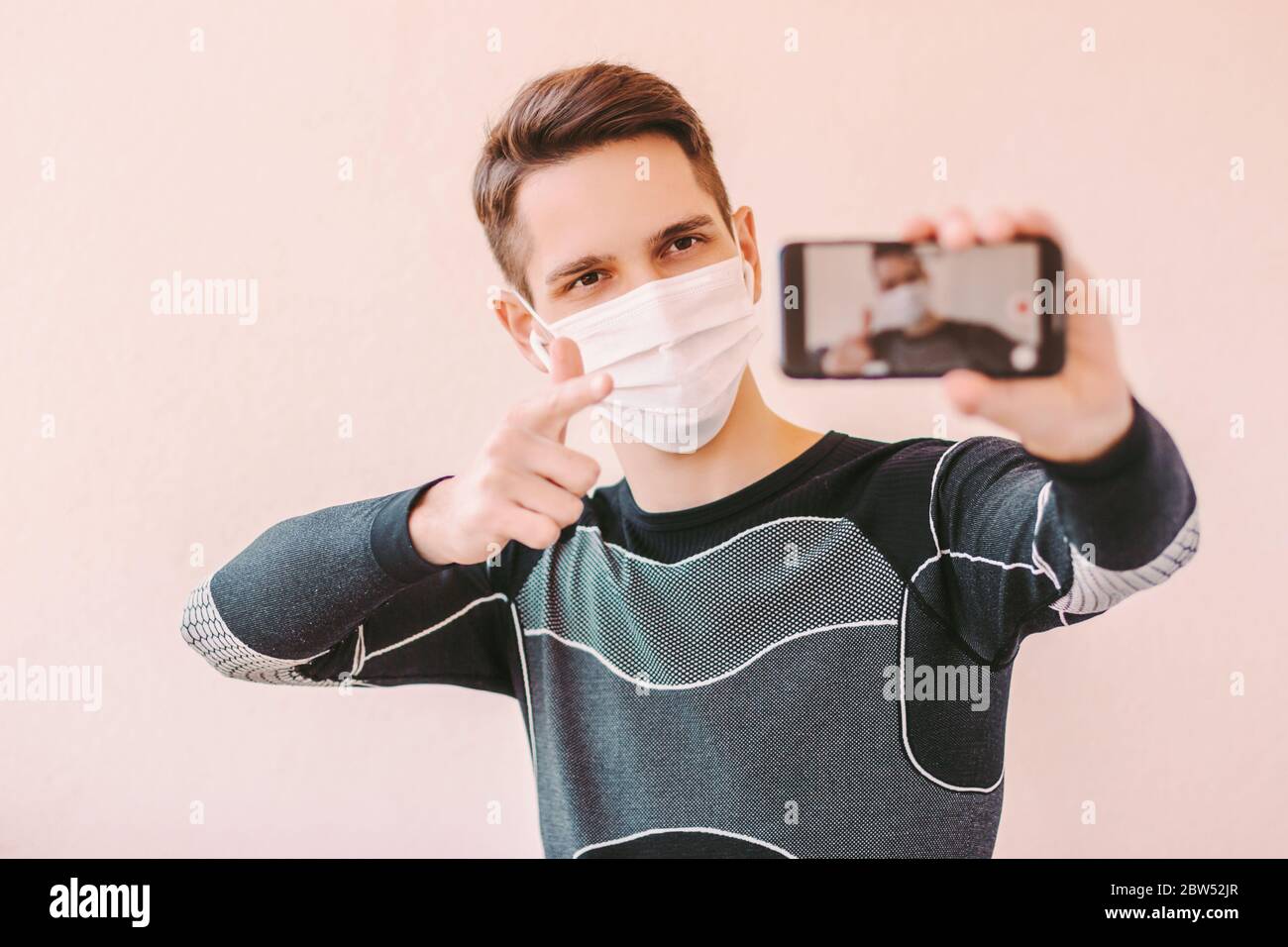 Homme confiant entraîneur de forme physique dans le masque médical de protection visage pointant vers la caméra de téléphone pour la motivation des abonnés. Jeune homme de sport blogueur influenceur r Banque D'Images