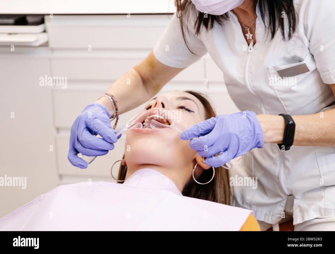 Dentiste méconnaissable en gants de latex utilisant un outil professionnel  pour examiner les dents de la jeune femme pendant le travail en clinique  moderne Photo Stock - Alamy