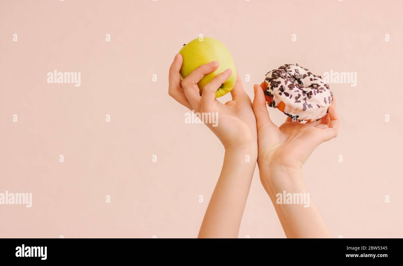 Gros plan femme de fitness tenant la pomme fraîche et le donut doux dans les mains contre le fond avec l'espace de copie. Sport de forme femme choisir entre saine et j Banque D'Images