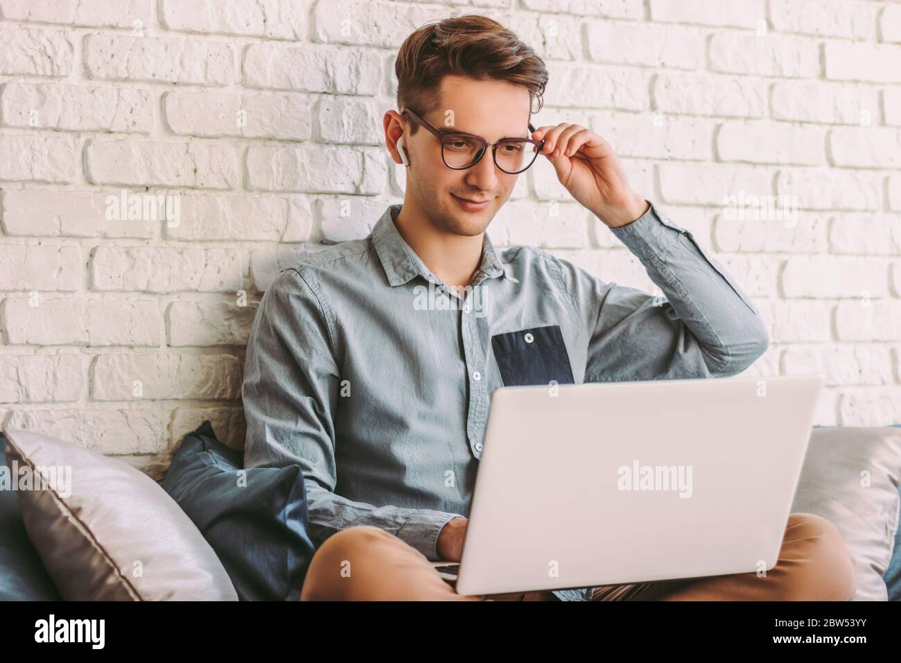 Homme d'affaires élégant indépendant travaillant sur ordinateur portable, surfer sur Internet sur canapé. Jeune homme hipster heureux portant des lunettes, en utilisant pc ordinateur pour dis Banque D'Images