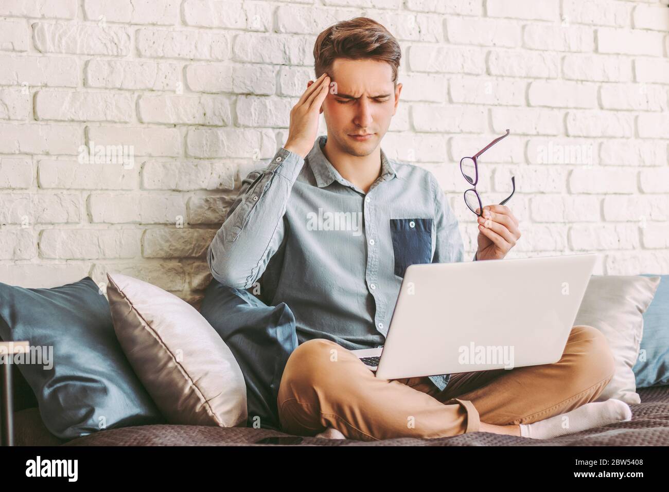 Jeune hippster stressé freelance homme de sentir mal de tête en travaillant avec un ordinateur portable à la maison. Un homme d'affaires frustré et fatigué s'assoit sur un canapé avec un ordinateur sur l Banque D'Images