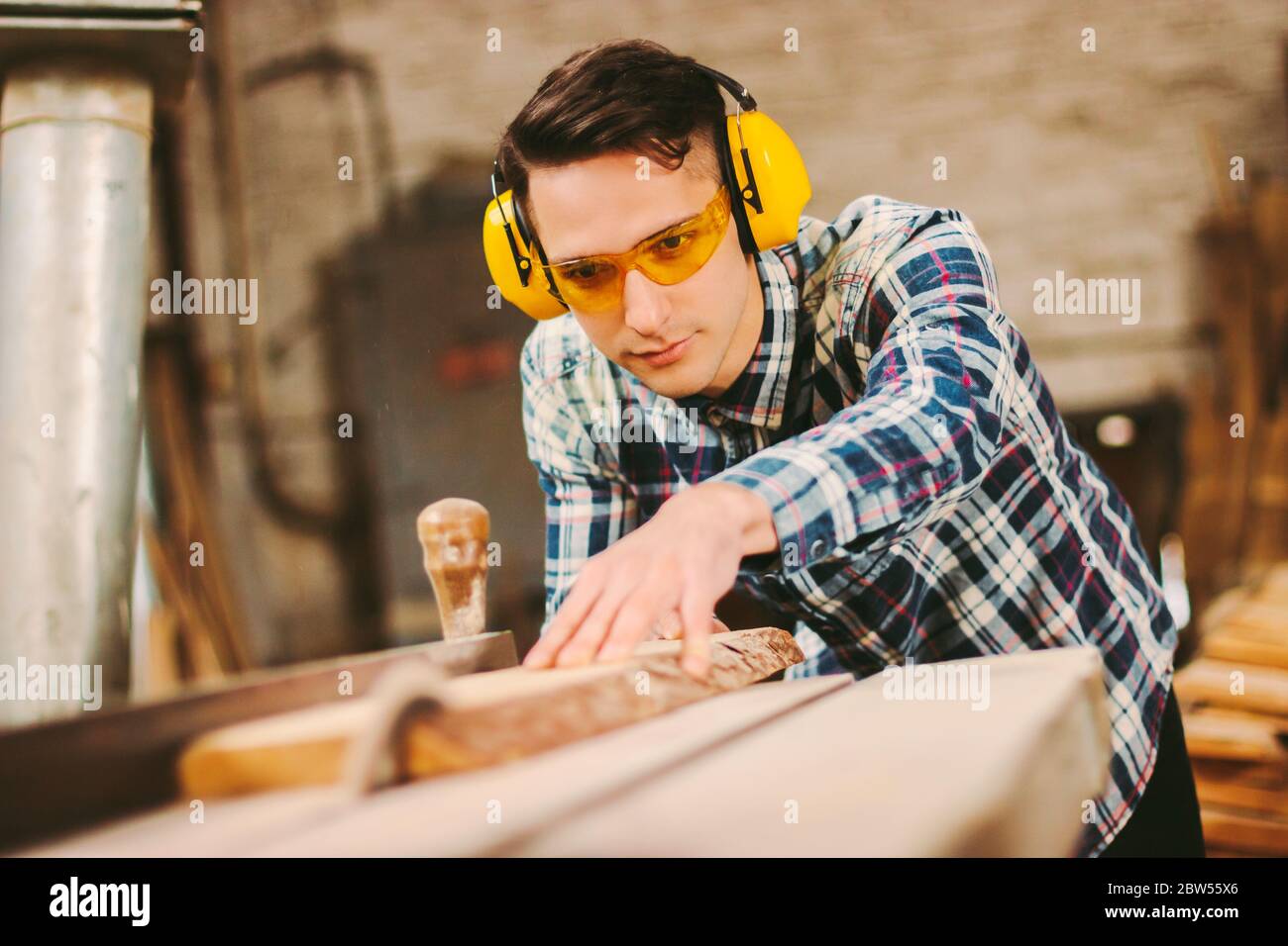 Fabricant d'armoires professionnel spécialisé dans les casques et lunettes de protection travaillant avec une scie dans un atelier de travail du bois. Menuisier mâle utilisant elec Banque D'Images
