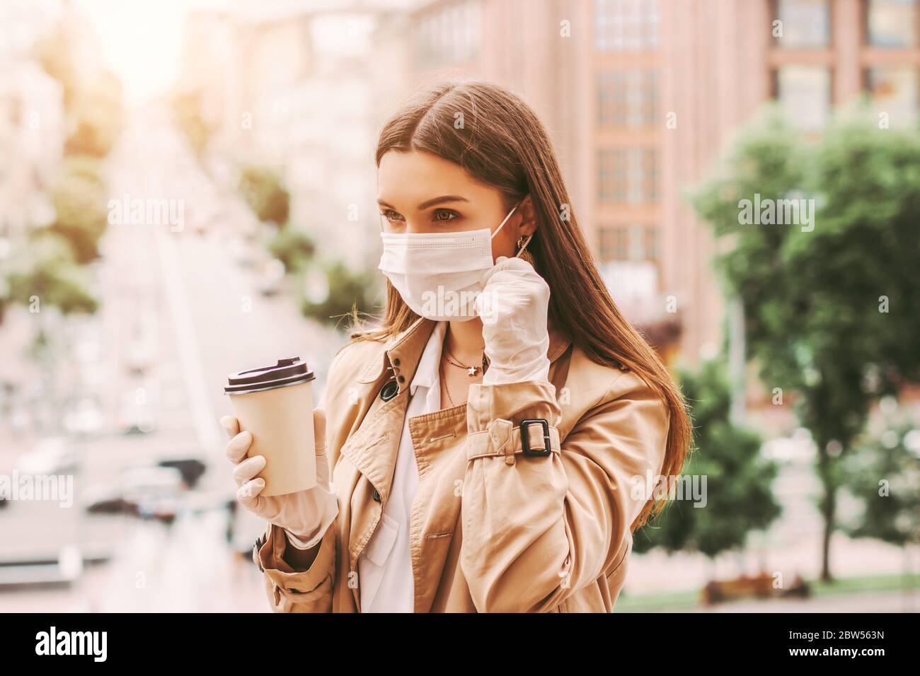 Femme élégante en masque médical, gants de protection boire un café à emporter dans la rue. Branché hipster fille dans le masque de protection, gants médicaux avec Banque D'Images