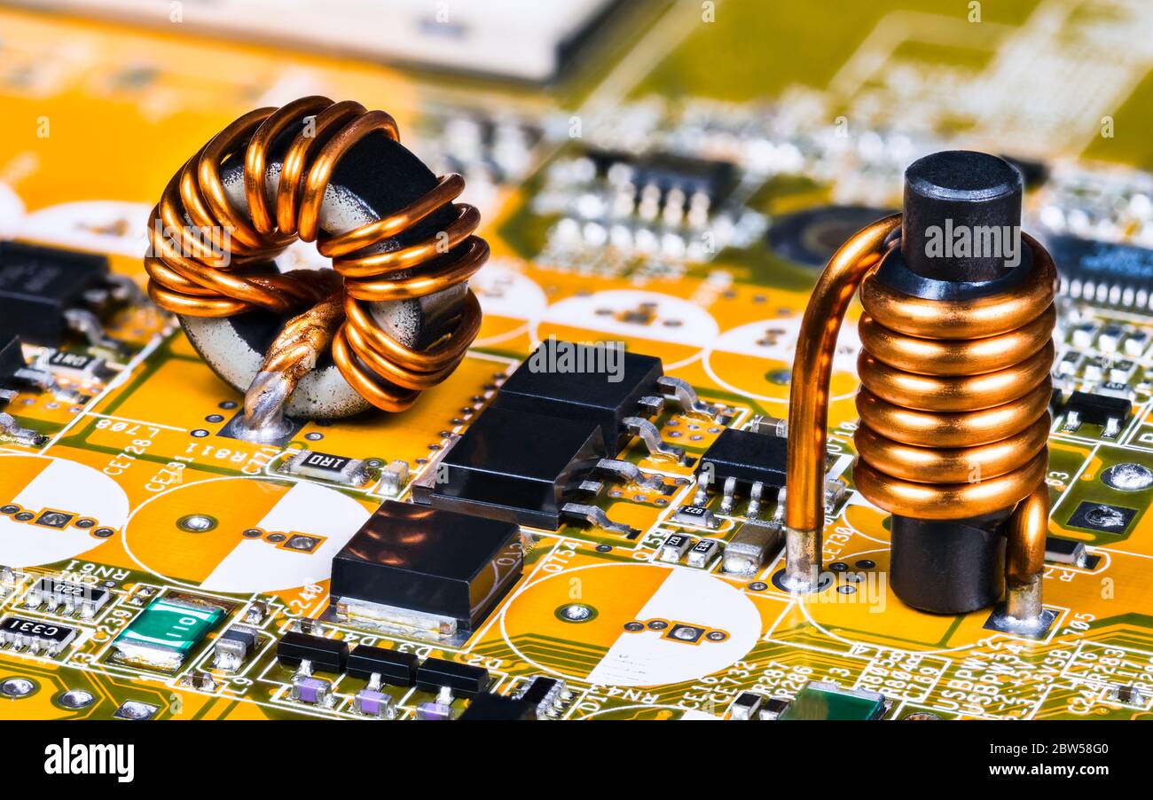 Inductance toroïdale et cylindrique sur la carte de circuit imprimé de la carte-mère de l'ordinateur. Bobines à induction soudées avec bobinage de fil de cuivre, puces, transistors. Banque D'Images