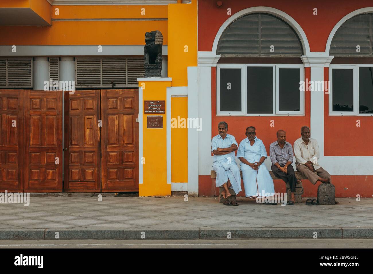 Quatre hommes sont assis sur un banc devant les bâtiments colorés de l'époque coloniale française à White Town, Pondichéry, Inde Banque D'Images