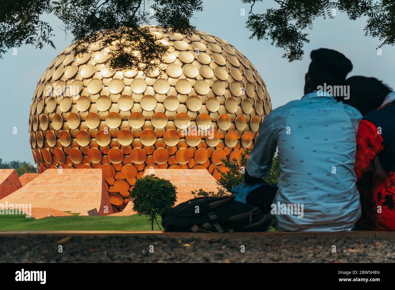 Un couple indien se détend devant Matrimandir, une structure sphérique dorée construite pour la méditation dans le canton expérimental d'Auroville, en Inde Banque D'Images