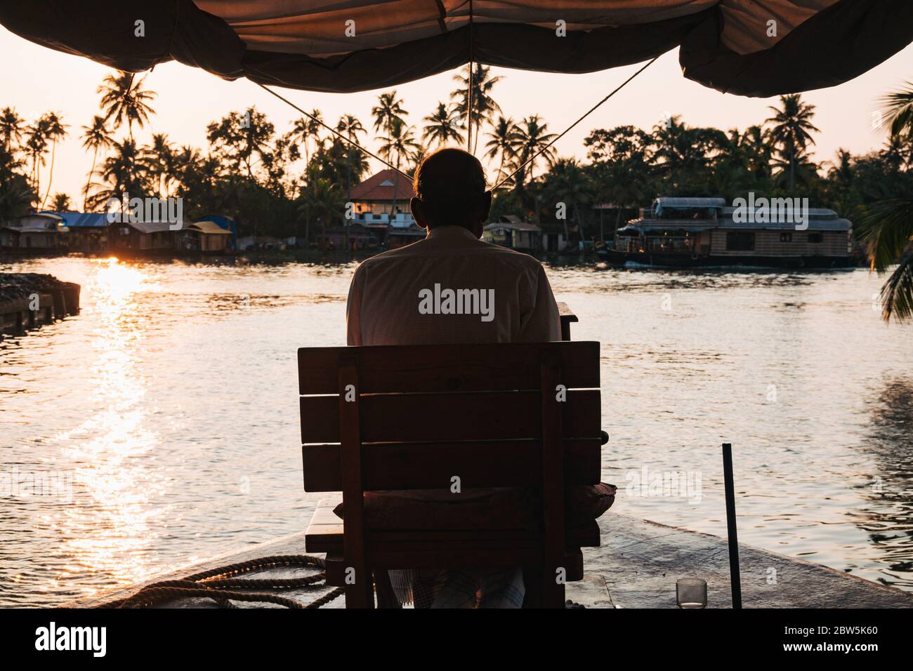 Le conducteur d'une péniche Keralan dirige le bateau depuis un siège sur l'arc, au coucher du soleil Banque D'Images