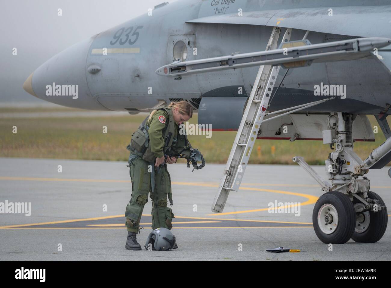 Saint John (Nouveau-Brunswick), Canada - le 17 septembre 2017 : une pilote de chasse féminine prépare sa combinaison de vol debout à côté d'un avion de chasse CF-18 Hornet. Banque D'Images