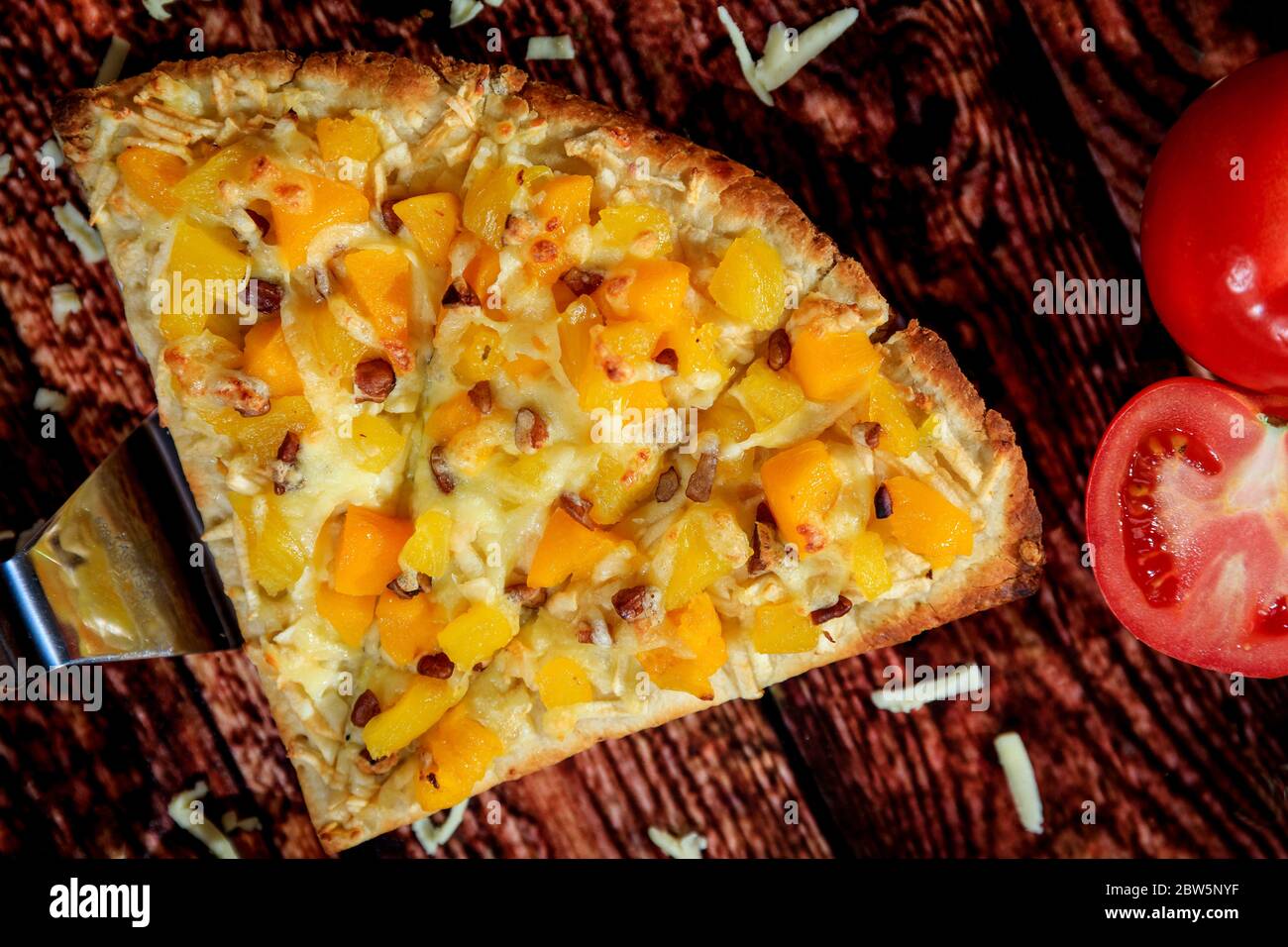 Vue de près et de dessus d'une pizza spéciale avec mangue et ananas, accompagnée d'une saucisse chaude sur une table en bois Banque D'Images