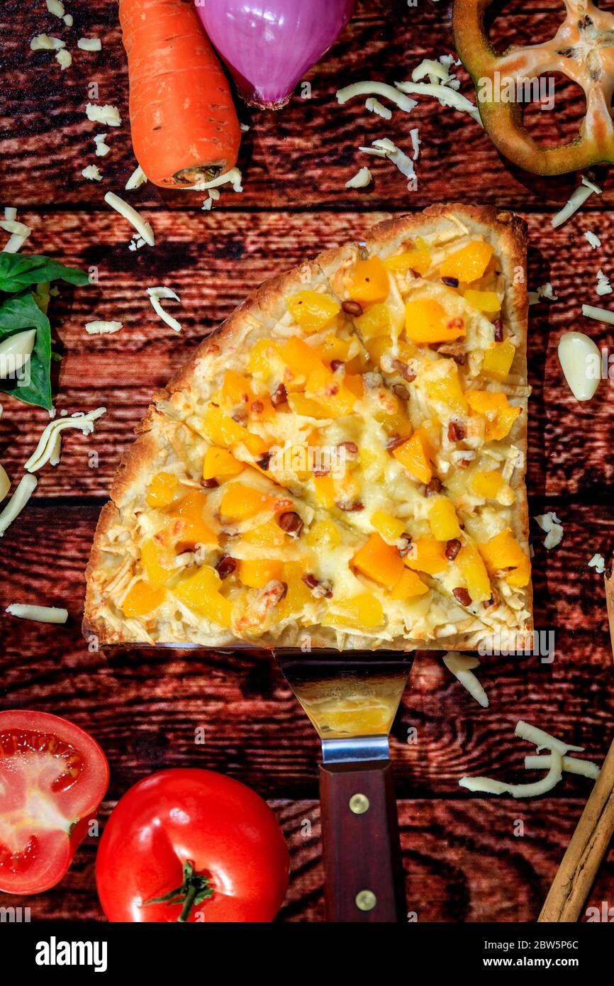 Vue de dessus de la tranche de pizza aux saveurs contrastées avec saucisse chaude et ananas doux et mangue entourée de légumes frais sur une table en bois sombre Banque D'Images