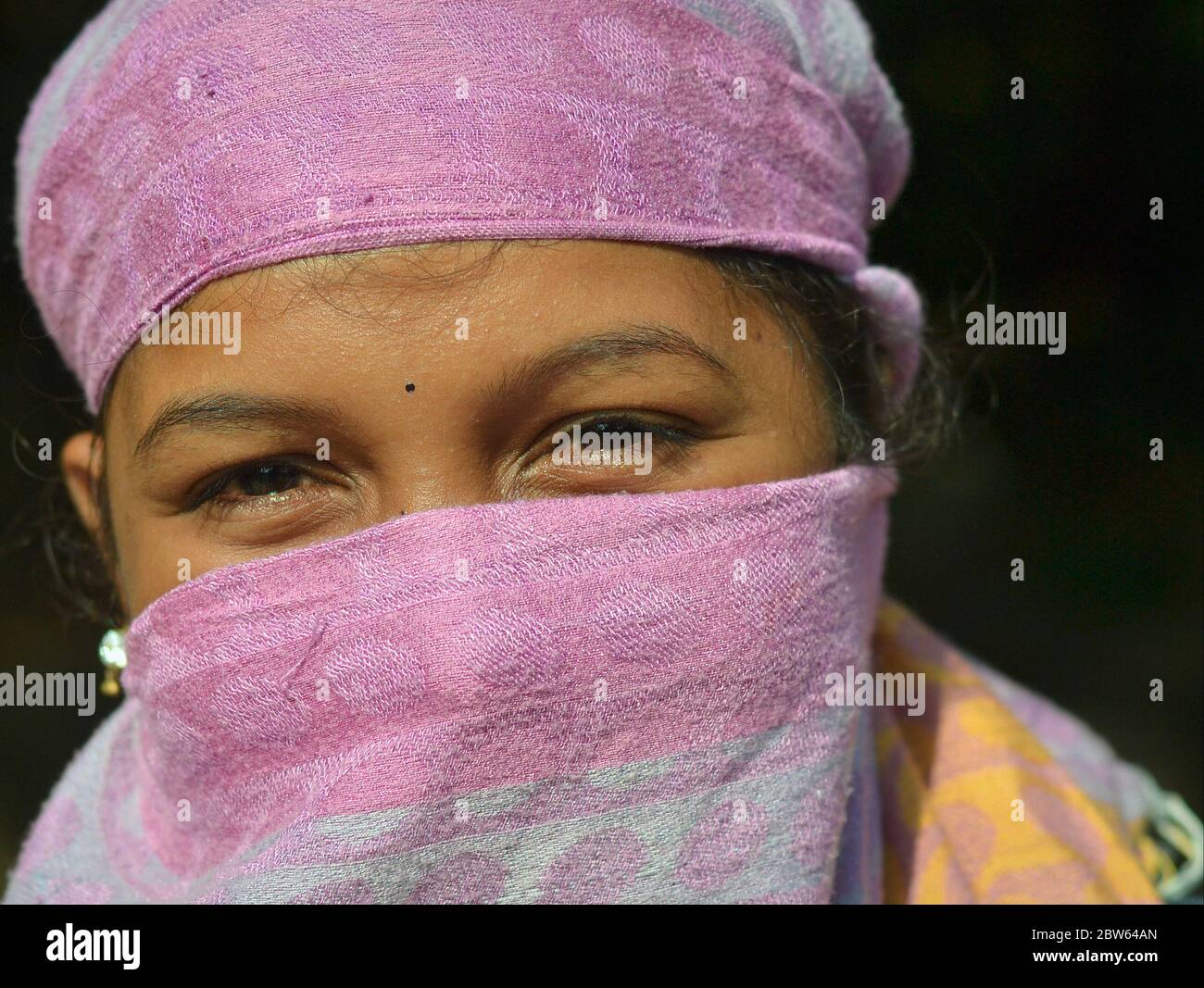 Une jeune femme indienne aux yeux magnifiques recouvre son nez et sa bouche avec un voile de poussière mauve. Banque D'Images