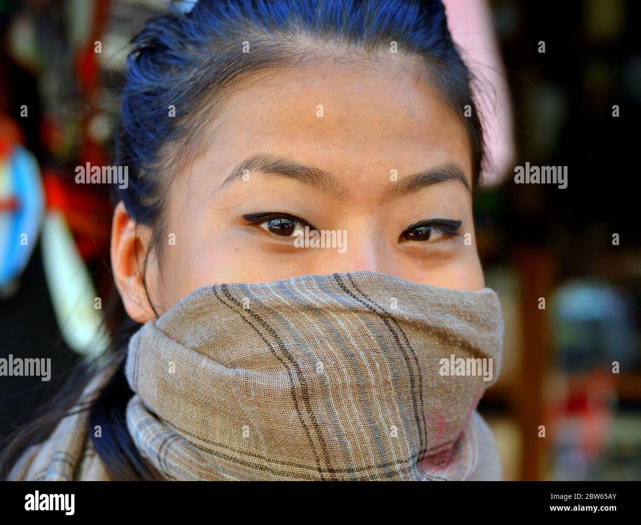Une jeune femme angami indienne aux yeux magnifiques couvre son nez et sa bouche avec un foulard protecteur. Banque D'Images