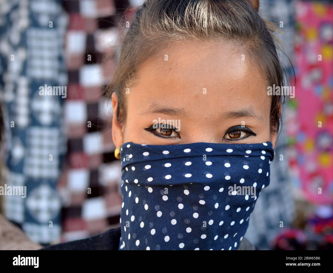 Une jeune femme angami indienne aux yeux magnifiques couvre la partie inférieure de son visage avec un voile de poussière bleu à pois. Banque D'Images