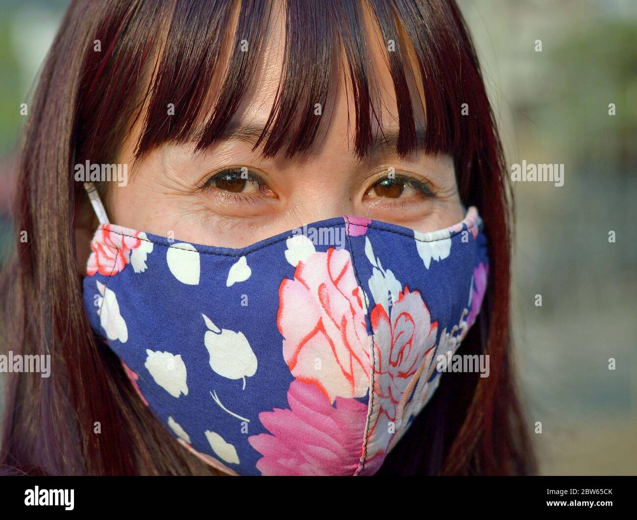 Femme asiatique mûre avec de beaux yeux bruns couvre son nez et sa bouche avec un masque facial contour d'oreille lavable. Banque D'Images