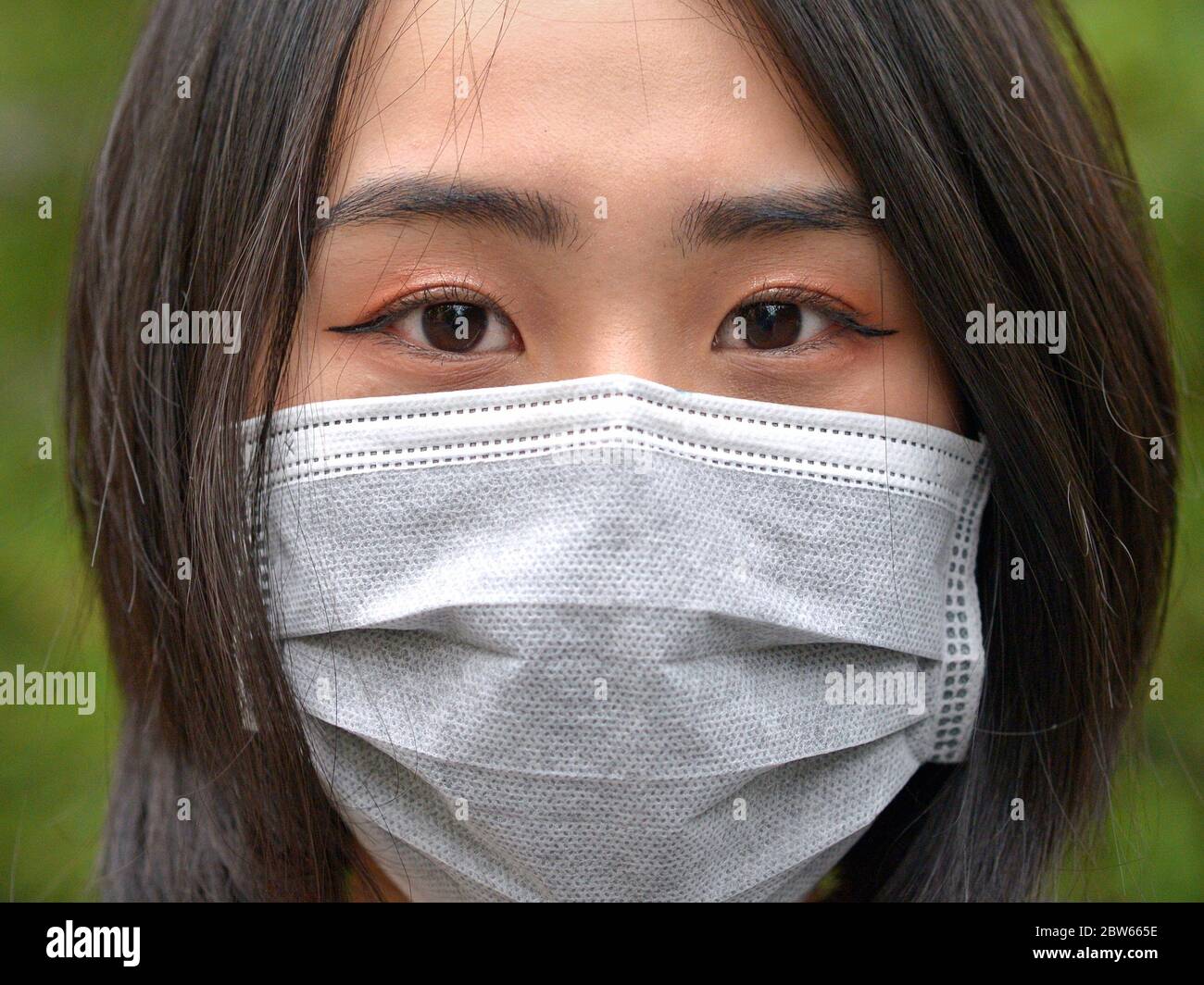 Une jeune femme vietnamienne aux yeux magnifiques porte un masque facial jetable chirurgical pendant la pandémie de 2019/20 du virus corona. Banque D'Images