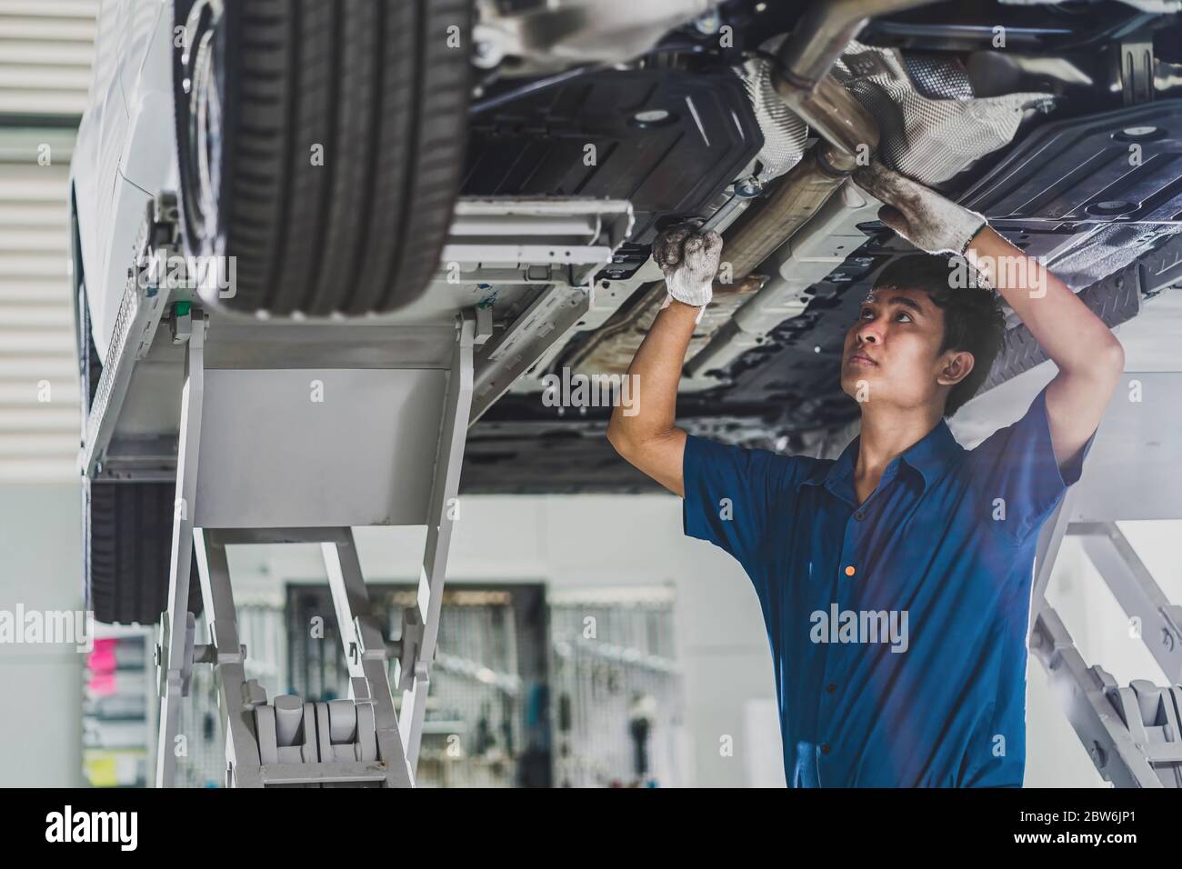 Réparation mécanique asiatique et éclairage sous la voiture dans le centre de service de maintenance qui fait partie du showroom, technicien ou ingénieur professionnel Banque D'Images
