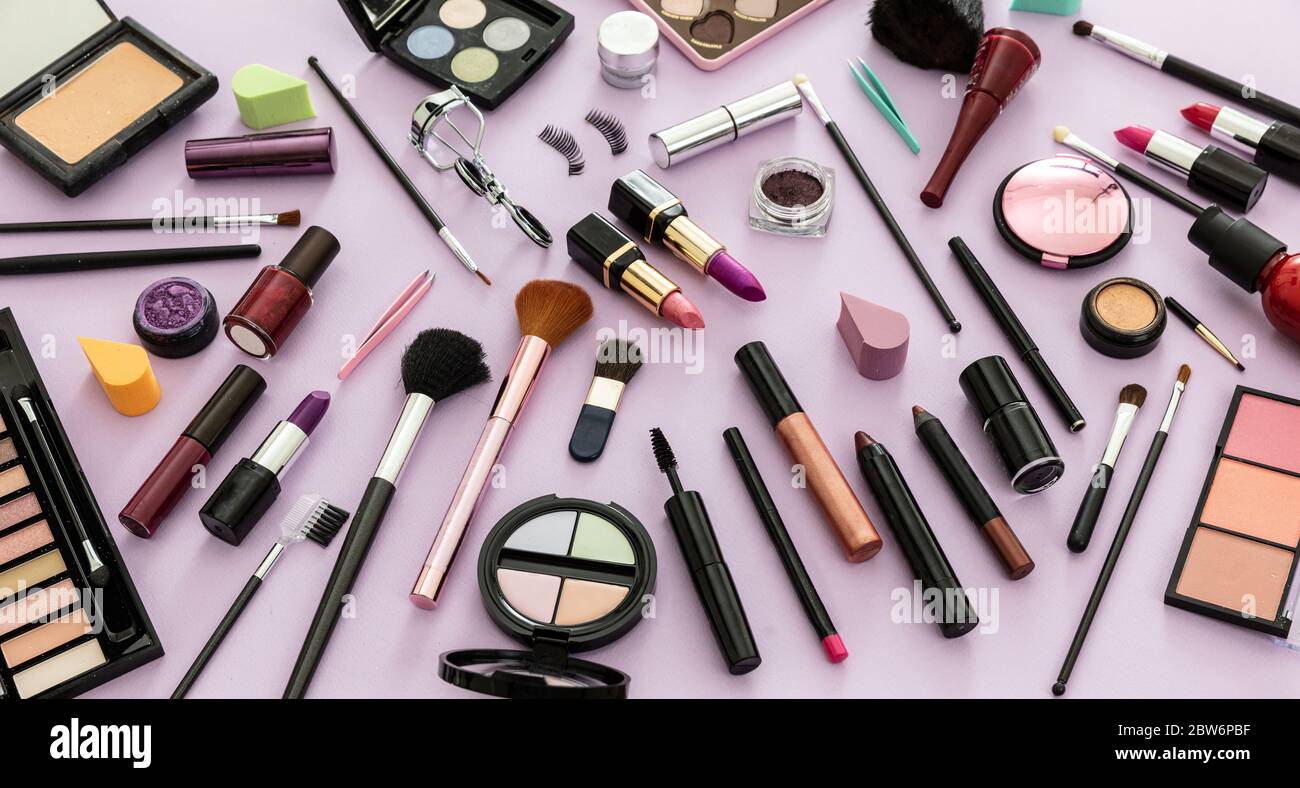 Maquillage cosmétiques plat. Rouge à lèvres et vernis à ongles, ombres à paupières et blush, brosses et crayons sur fond violet pastel Banque D'Images