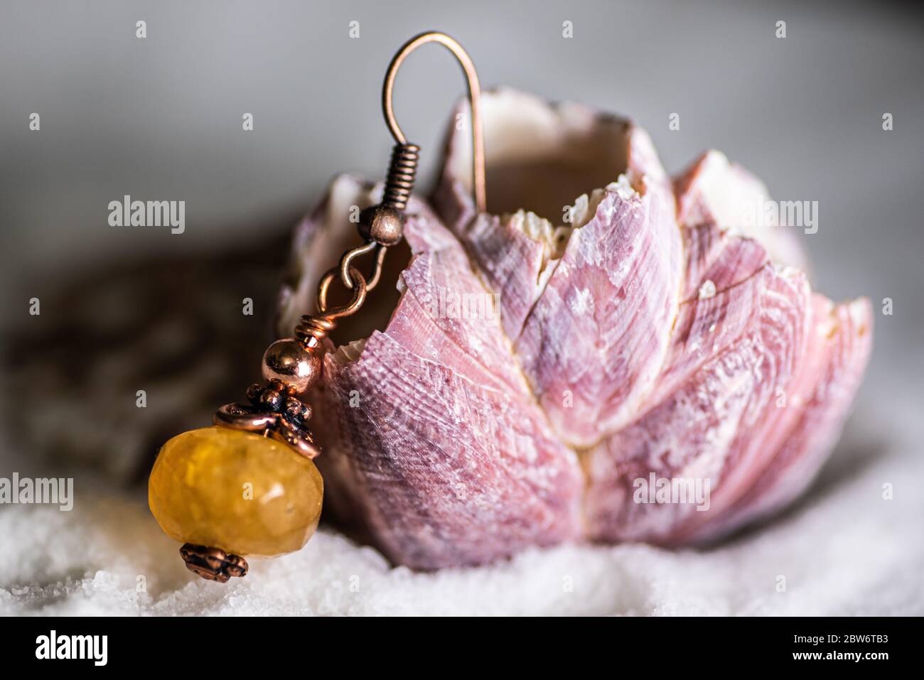 Boucles d'oreilles faites main au miel et au jade et en laiton sur un joli coquillage rose, assis sur du sable Banque D'Images