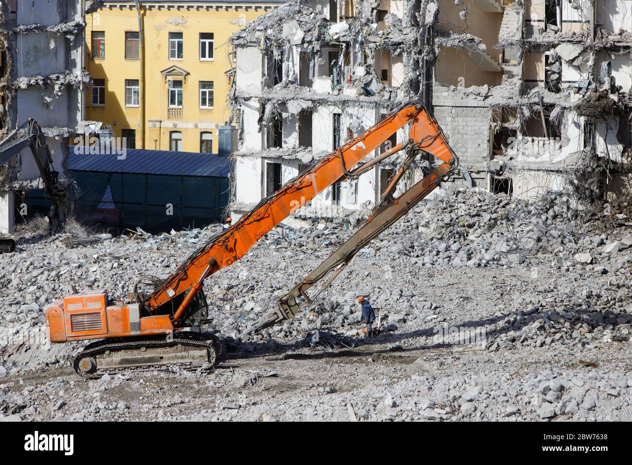 Démolition de bâtiments avec une pelle hydraulique-destructeur pour travaux en haute altitude. Saisir la grue avec des ciseaux hydrauliques. Structures en béton armé. Banque D'Images