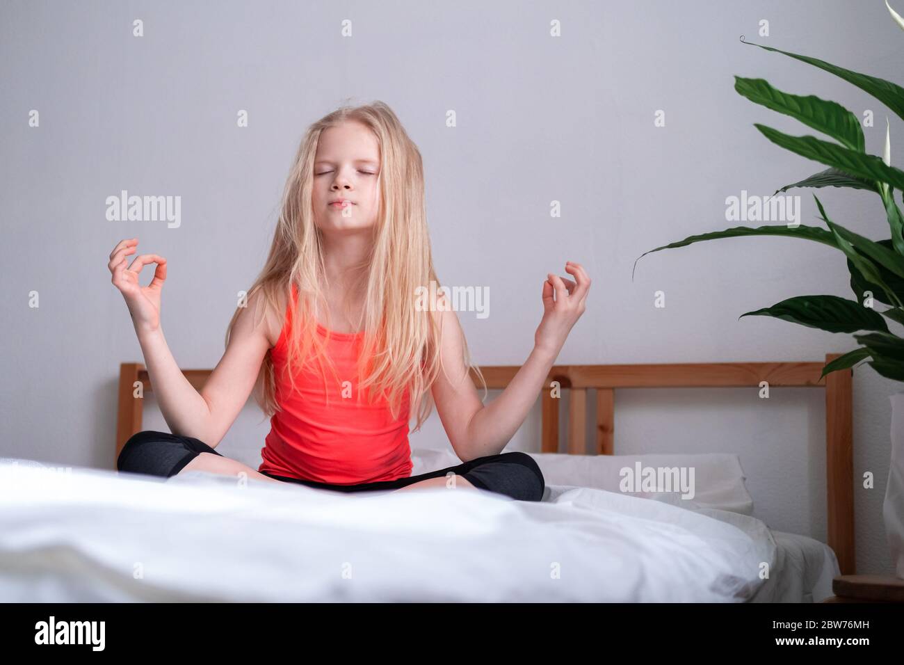 Petite fille Blonde est engagée dans la méditation et le yoga, l'exercice à la maison, position assise de lotus sur le lit. Détente Banque D'Images