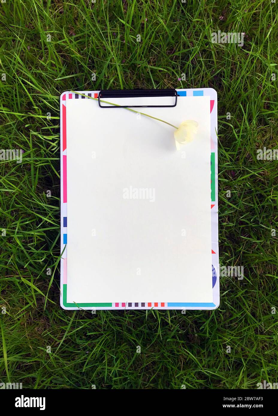 Photo du presse-papiers avec une feuille de papier vierge sur herbe verte, vue du dessus. Banque D'Images