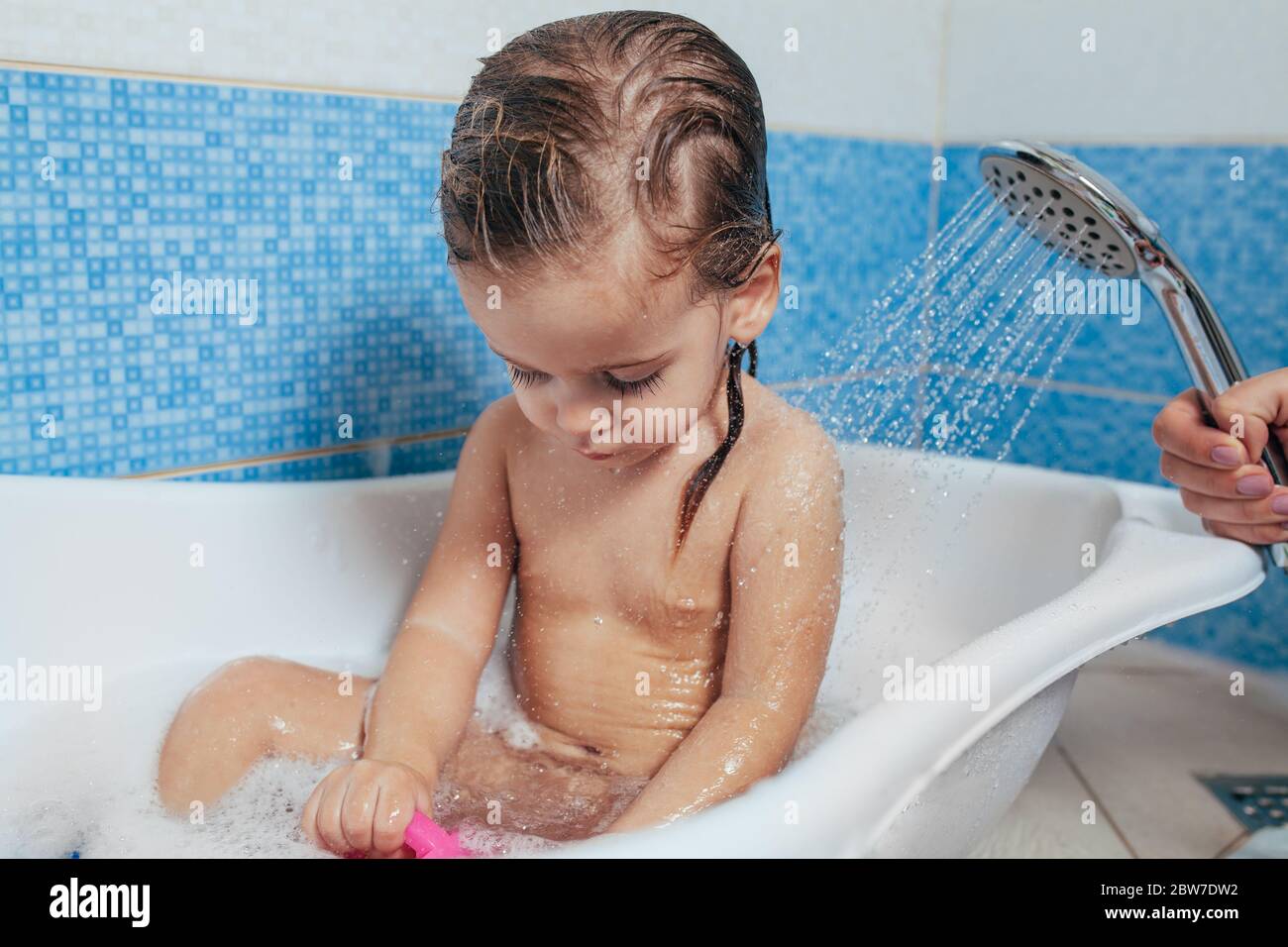 Belle petite fille prendre un bain à la maison. Un mignon bébé est assis  dans la salle de bains et de jouer avec des jouets et de l'eau. L'hygiène  personnelle pour les