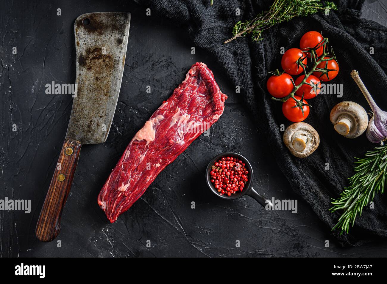 Machette biologique ou steak de jupe près du couteau de boucher avec poivre  rose et romarin. Arrière-plan noir. Vue de dessus Photo Stock - Alamy