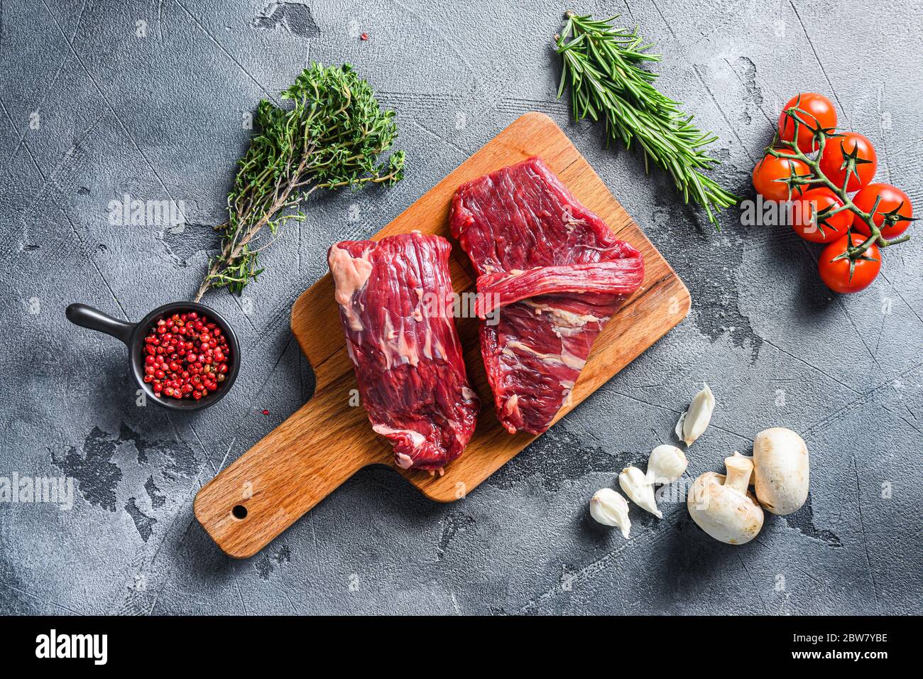 Steak à rabat cru coupé avec machette, steak de jupe, sur planche à découper en bois, avec tomates fines grains de poivre sur fond gris de surface de pierre vi Banque D'Images