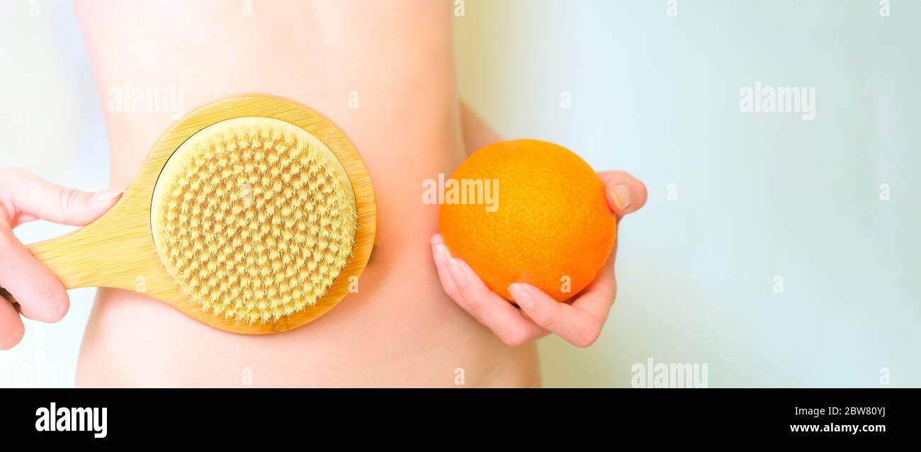 Femme porte une brosse orange et une brosse de massage. Massage anti cellulite et perte de poids. Femme avec une forme parfaite sur fond bleu pastel. Banque D'Images