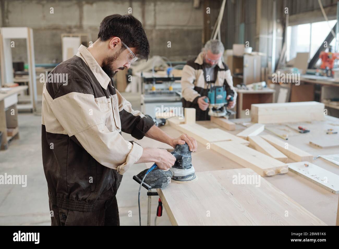 Jeune ouvrier d'usine utilisant une meuleuse pour rendre la surface de la pièce lisse et préparer le bois en vue d'un traitement ultérieur Banque D'Images