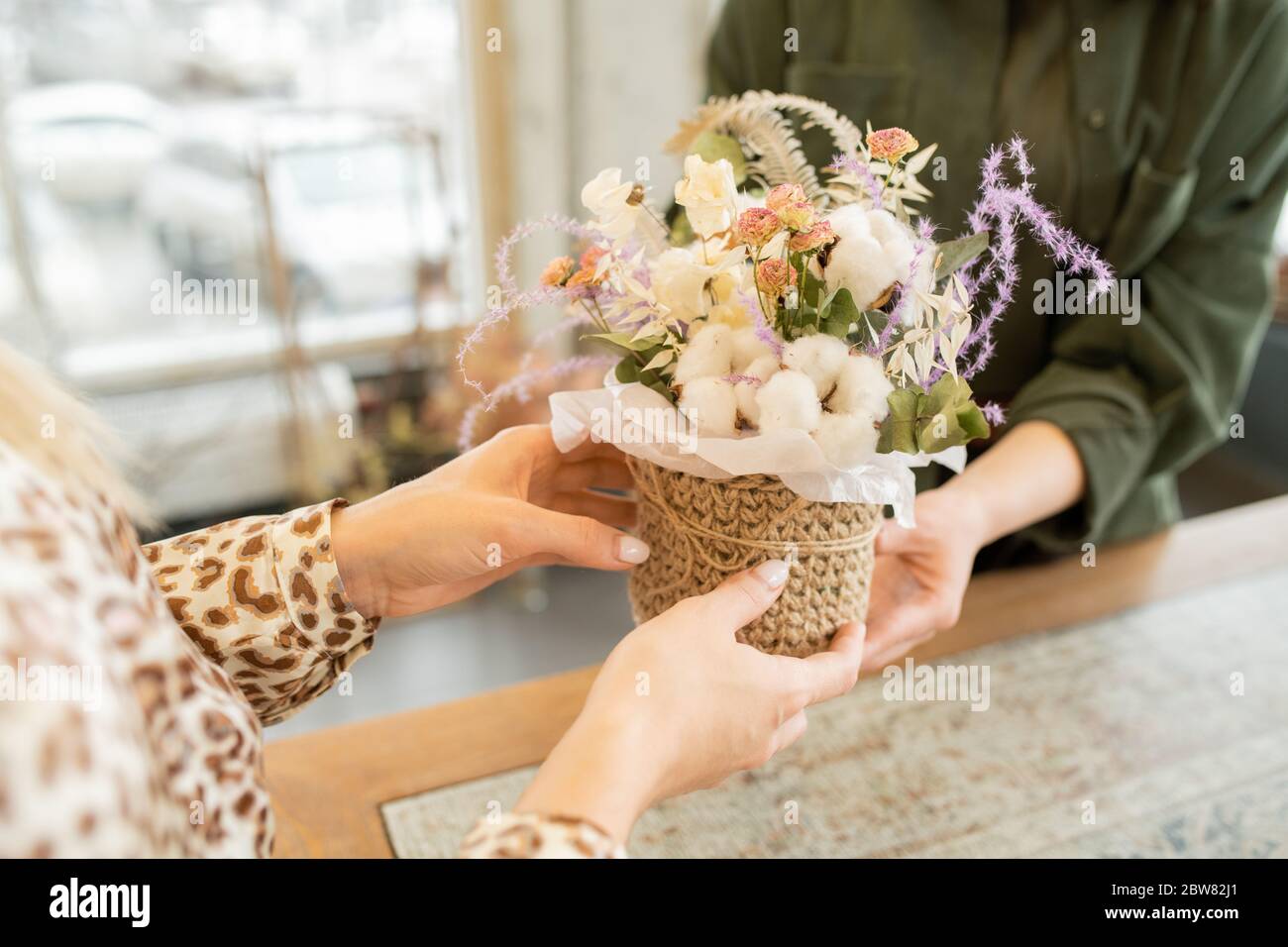 Mains de jeune femme prenant petit panier avec bouquet floral tout en visitant boutique florististe pour acheter des fleurs pour son ami ou sa mère Banque D'Images