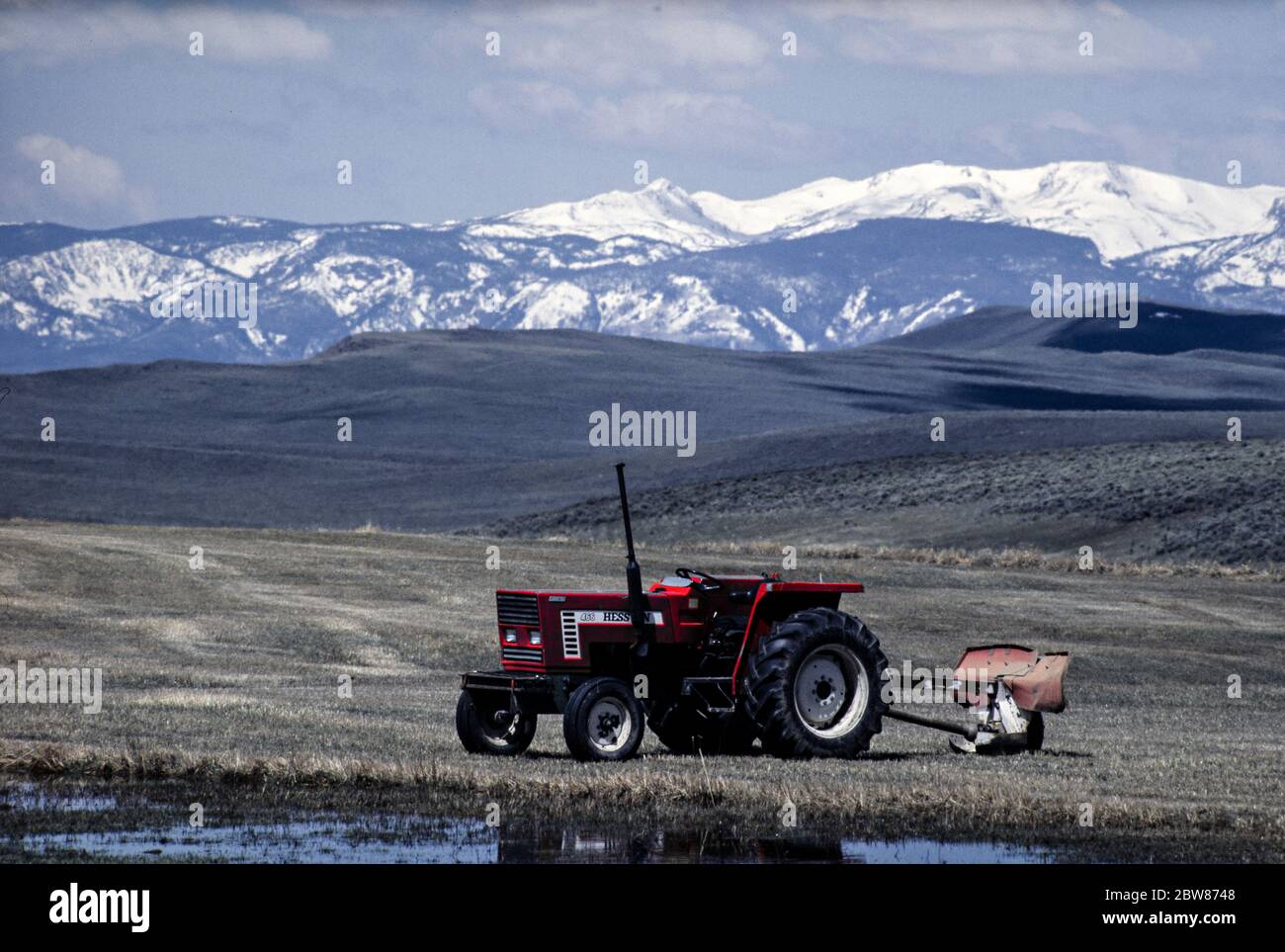 Un tracteur et une charrue rouges abandonnés près de Gould, Colorado, dans les montagnes Rocheuses, aux États-Unis, avec des montagnes enneigées en arrière-plan Banque D'Images