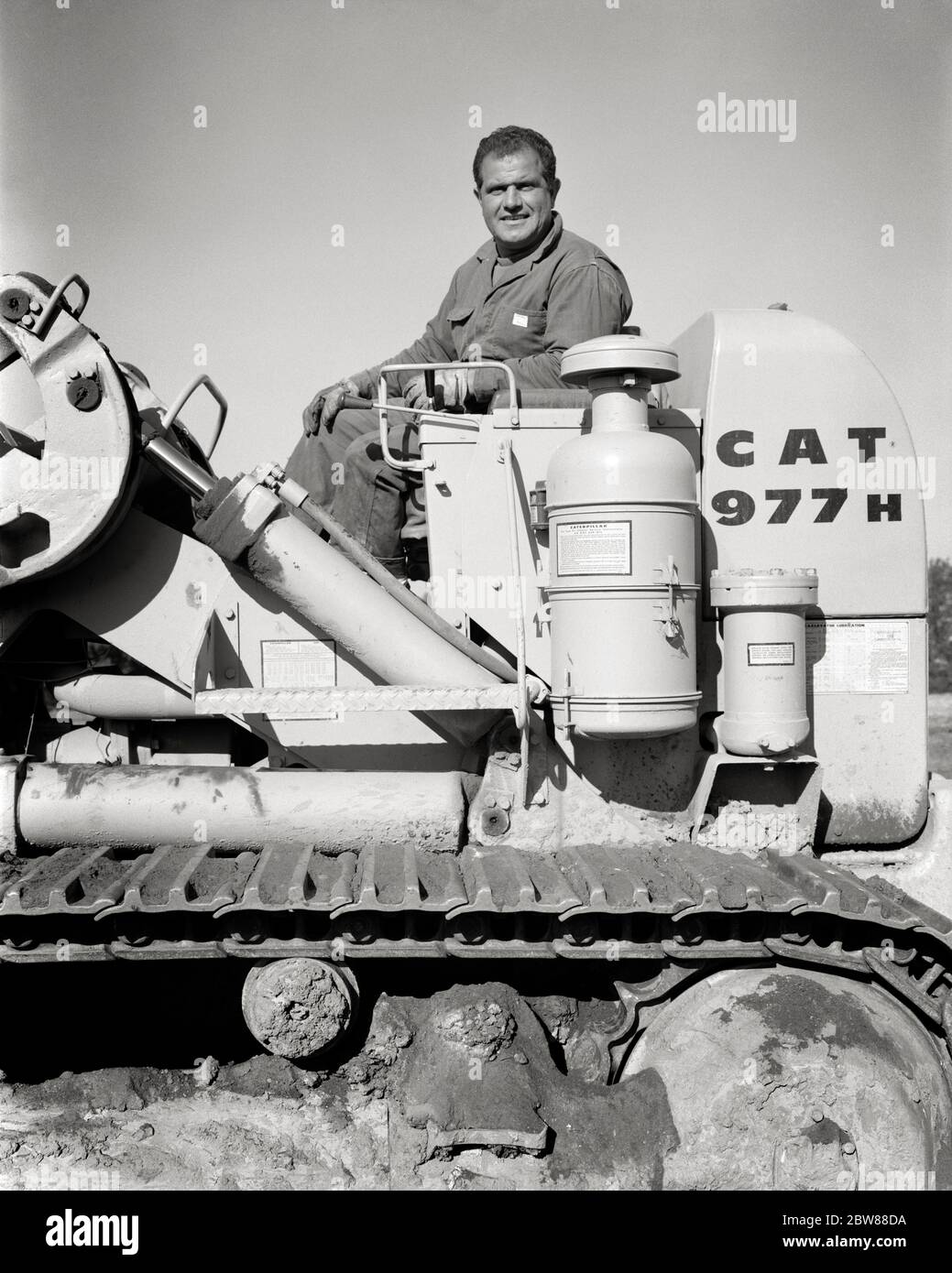 ANNÉES 1960 HOMME SOURIANT CONDUCTEUR D'ÉQUIPEMENT DE CONSTRUCTION REGARDANT LA CAMÉRA ASSIS SUR LA CONDUITE CATERPILLAR TERRASSEMENT BULDOZER - I4866 HAR001 HARS B&W HOMME D'ÂGE MOYEN CONTACT ŒIL BLEU COLLIER COMPÉTENCE MÉTIER PROFESSIONNEL CONDUCTEUR MANUEL FORCE BULLDOZER BAS ANGLE PUISSANT INDÉPENDANT FIERTÉ DU TRAVAIL SUR L'AUTORITÉ EMPLOIS CONCEPTUEL SÉPARÉ SOLITAIRE SEUL EMPLOYÉ SOLO COMMERCE CATERPILLAR ADULTE MOYEN ADULTE HOMME MOYEN-ADULTE NOIR ET BLANC RACE BLANCHE HAR001 TRAVAIL INDIVIDUEL ANCIEN MODE Banque D'Images