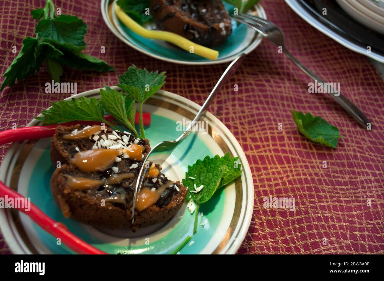 Un morceau de gâteau au chocolat et de bonbons en gelée colorés sur une assiette décorée de menthe, de copeaux de noix de coco et de lait condensé gros plan sur un dos Banque D'Images