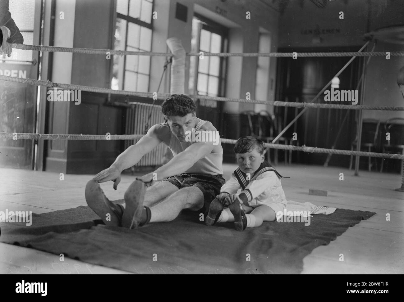 Le fils de Len Harvey visite le camp d'entraînement de son père pendant son entraînement pour le match du titre du monde . Len Harvey et Terry touchent les orteils sur le tapis ensemble . 18 juin 1932 Banque D'Images