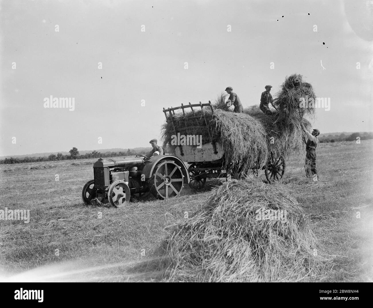 Les ouvriers agricoles de Farningham chargent du foin sur la remorque tractée par un tracteur . 1935 Banque D'Images