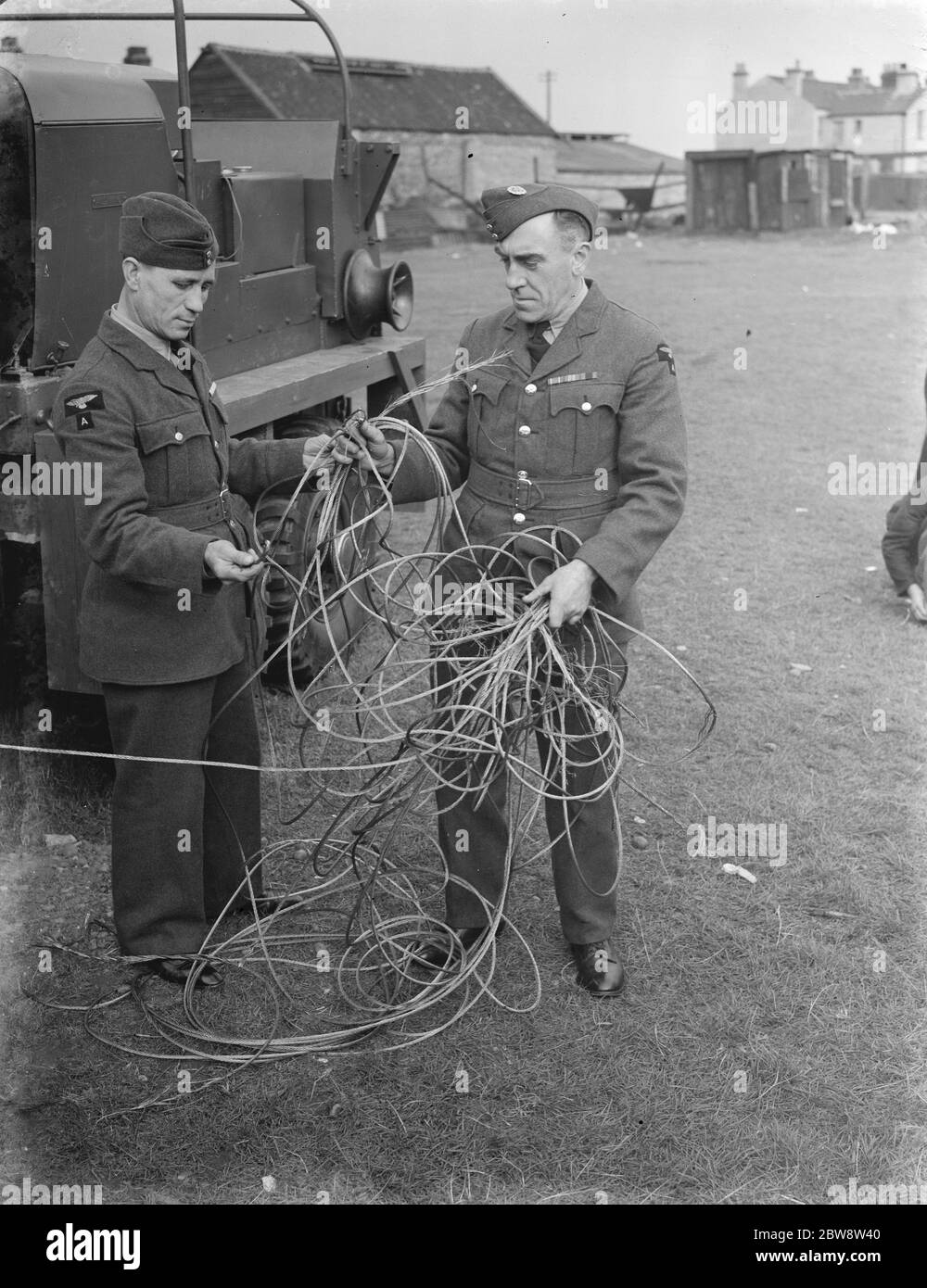 Deux hommes examinent les dommages causés par la tempête sous forme de câble cassé à une base de barrage à ballons . 1938 Banque D'Images