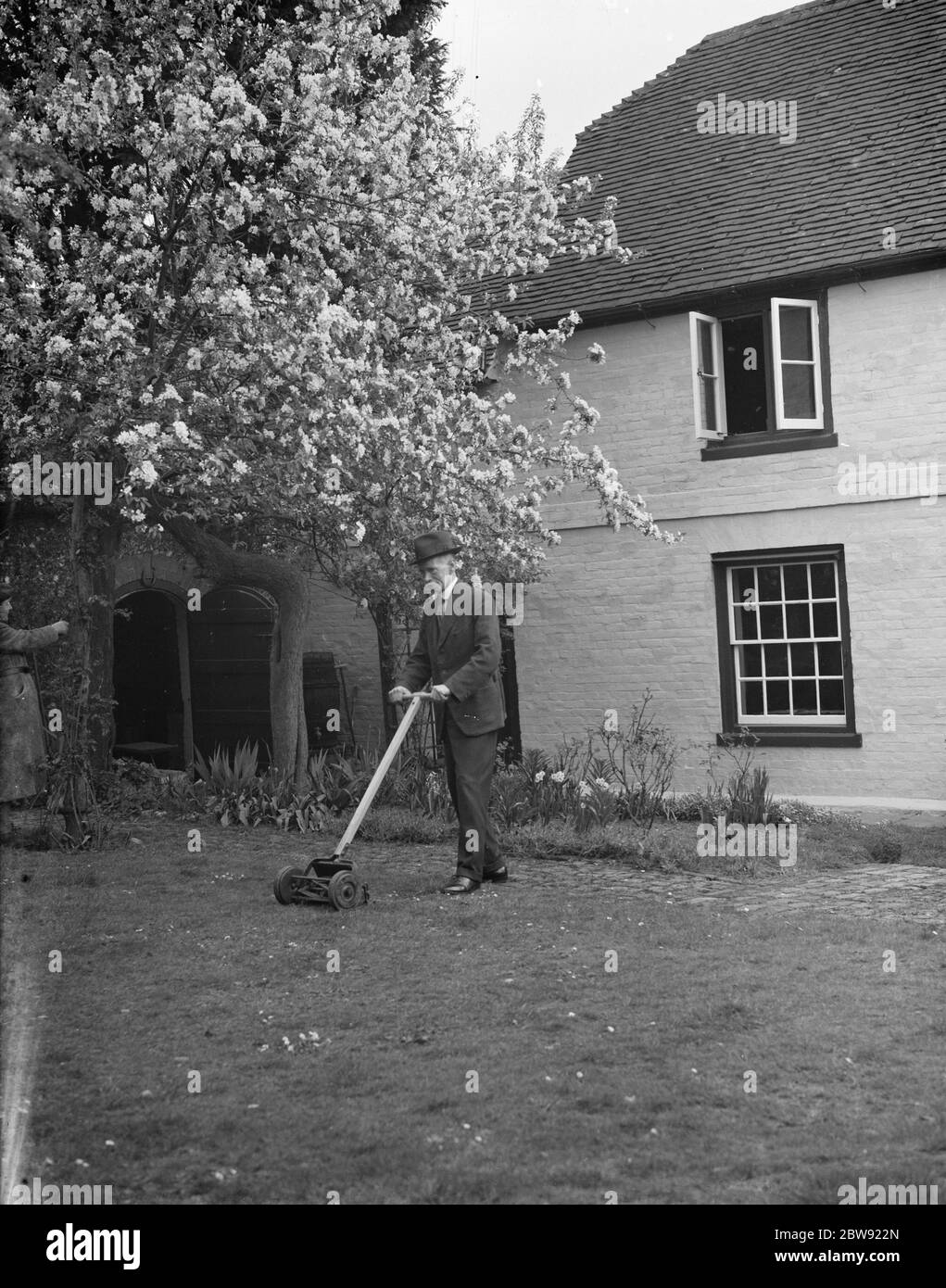 Un homme âgé coupe l'herbe dans son jardin de chalet à Farningham , Kent . 7 avril 1938 Banque D'Images