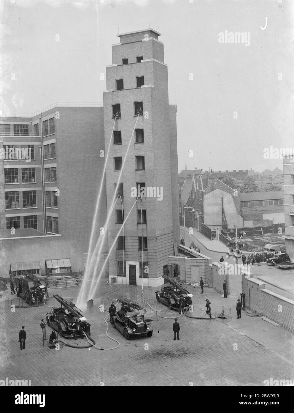 Un exposition de la brigade de pompiers de Londres à Lambeth , Londres . Les pompiers descendent des fenêtres d'un grand bâtiment démontrant la précision de leurs tuyaux en pulvérisant sur une plaque d'incendie au sol . 1939 Banque D'Images