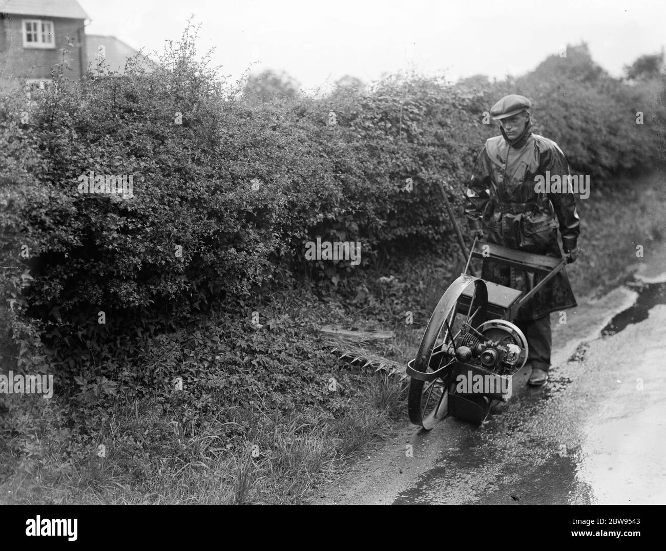 Un homme d'entretien utilise un scythe motorisé pour tondre le côté de la route . 1937 Banque D'Images