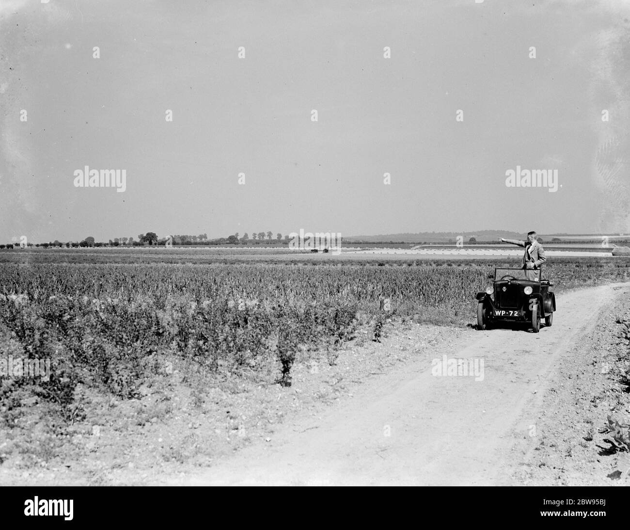 Un homme se tient dans sa voiture à toit ouvert , en prenant dans le paysage de campagne . 1936 Banque D'Images