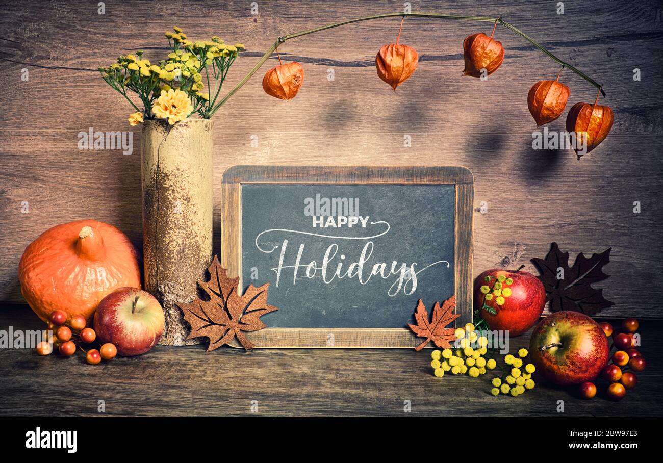 Décorations rustiques d'automne, texte « Hello Holidays » sur un tableau noir. Automne naturel récolte de Thanksgiving. Feuilles d'automne, couronne décorative à fleurs, baies et Banque D'Images