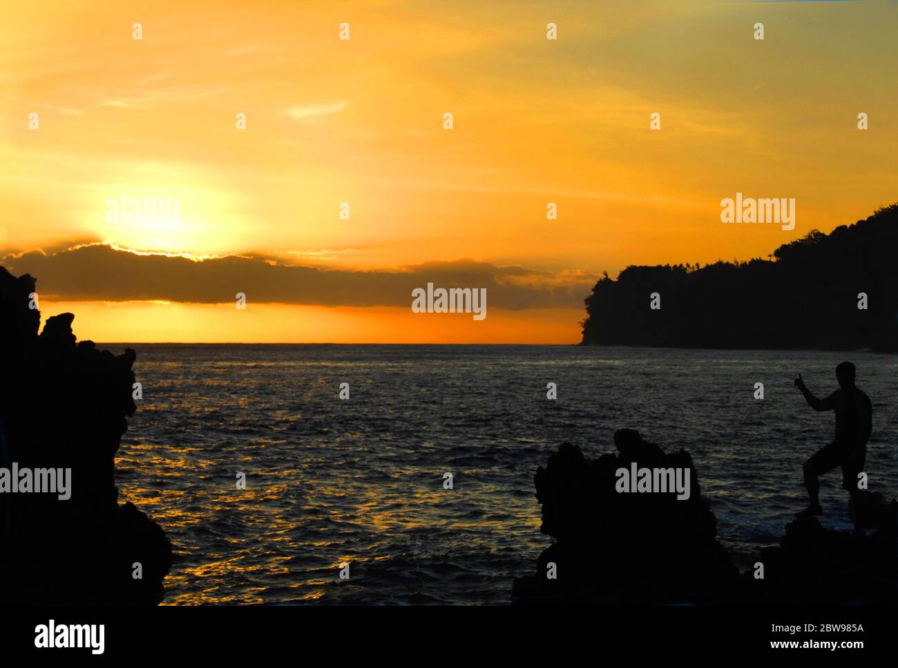 Hawaïen indigène monte les piles de mer jutantes de Laupahoehoe Beach Park. Il montre le coucher du soleil comme si pour encourager les autres à apprécier sa beauté. Banque D'Images