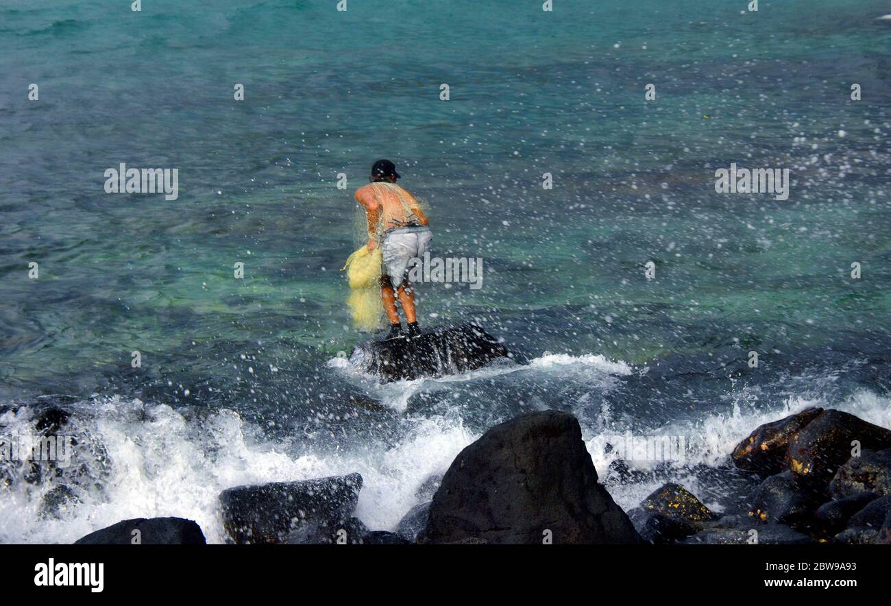 Pêcheur sur les rochers de la Grande île d'Hawaï croches prêt à jeter son filet de pêche. Il porte un chapeau, un short et des chaussures d'eau noires. Banque D'Images