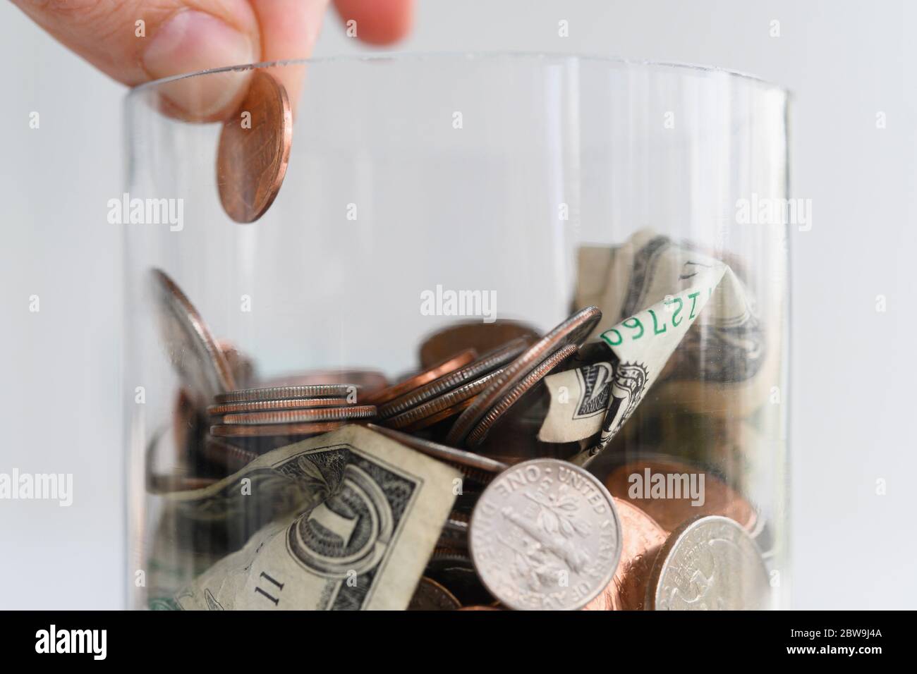 Gros plan des doigts mettant le cent américain dans le pot avec des pièces de monnaie et billets Banque D'Images