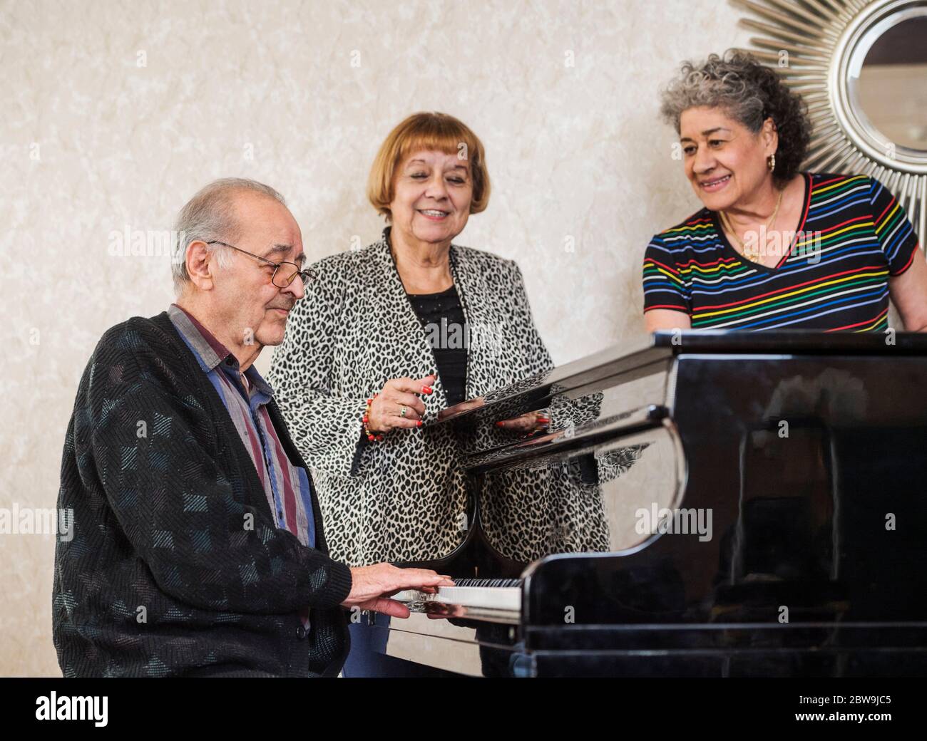 Femmes âgées écoutant un homme jouant du piano Banque D'Images