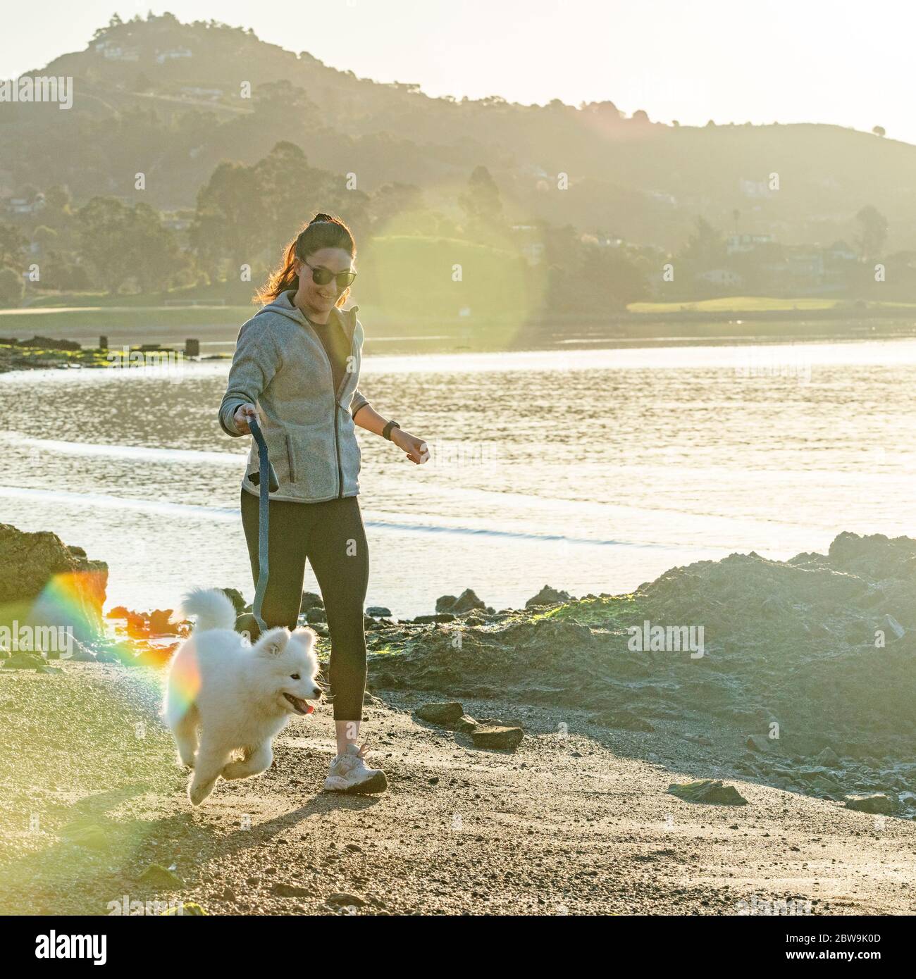 États-Unis, Californie, San Francisco, femme avec un chiot de Samoyed en train de courir sur la plage Banque D'Images