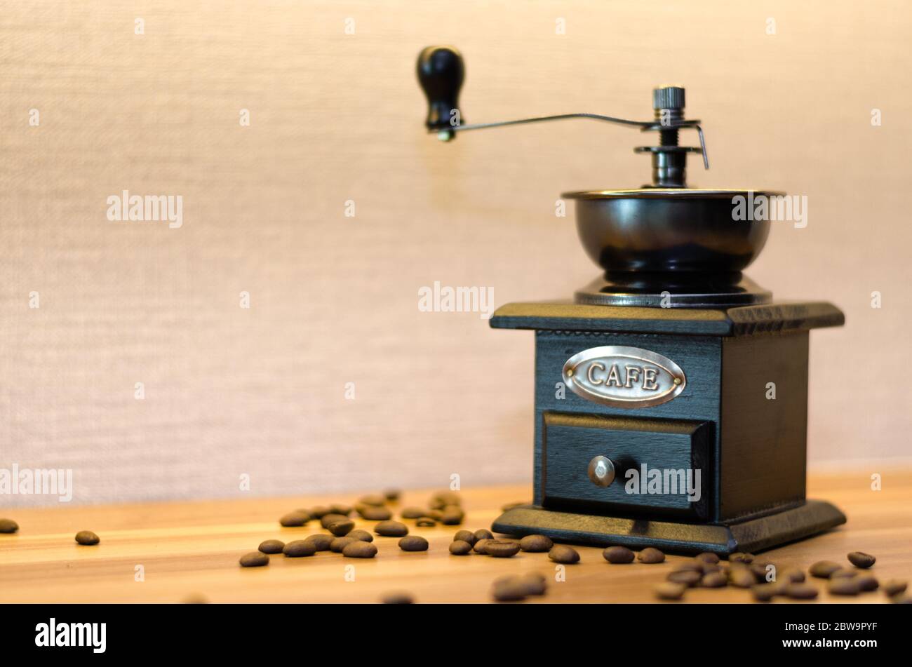 Un moulin à café avec un tiroir ouvert et des grains de café désordonnés sur une table en bois. Banque D'Images